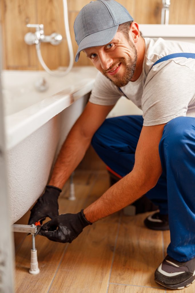 Cheerful plumber or technician smiling at camera while installing a bathtub in bathroom
